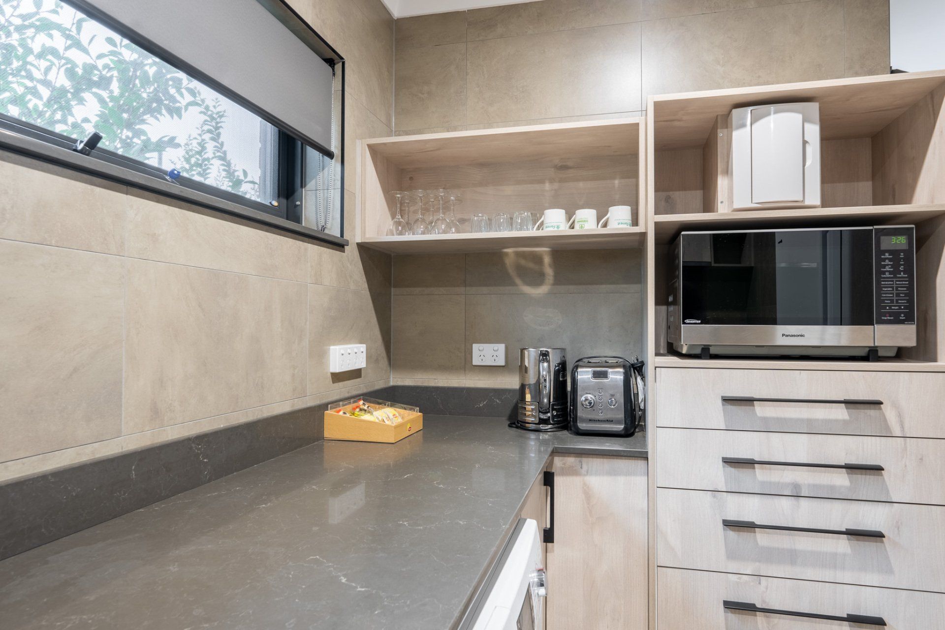 Modern kitchen counter with microwave, toaster, and shelves in a beige-toned room