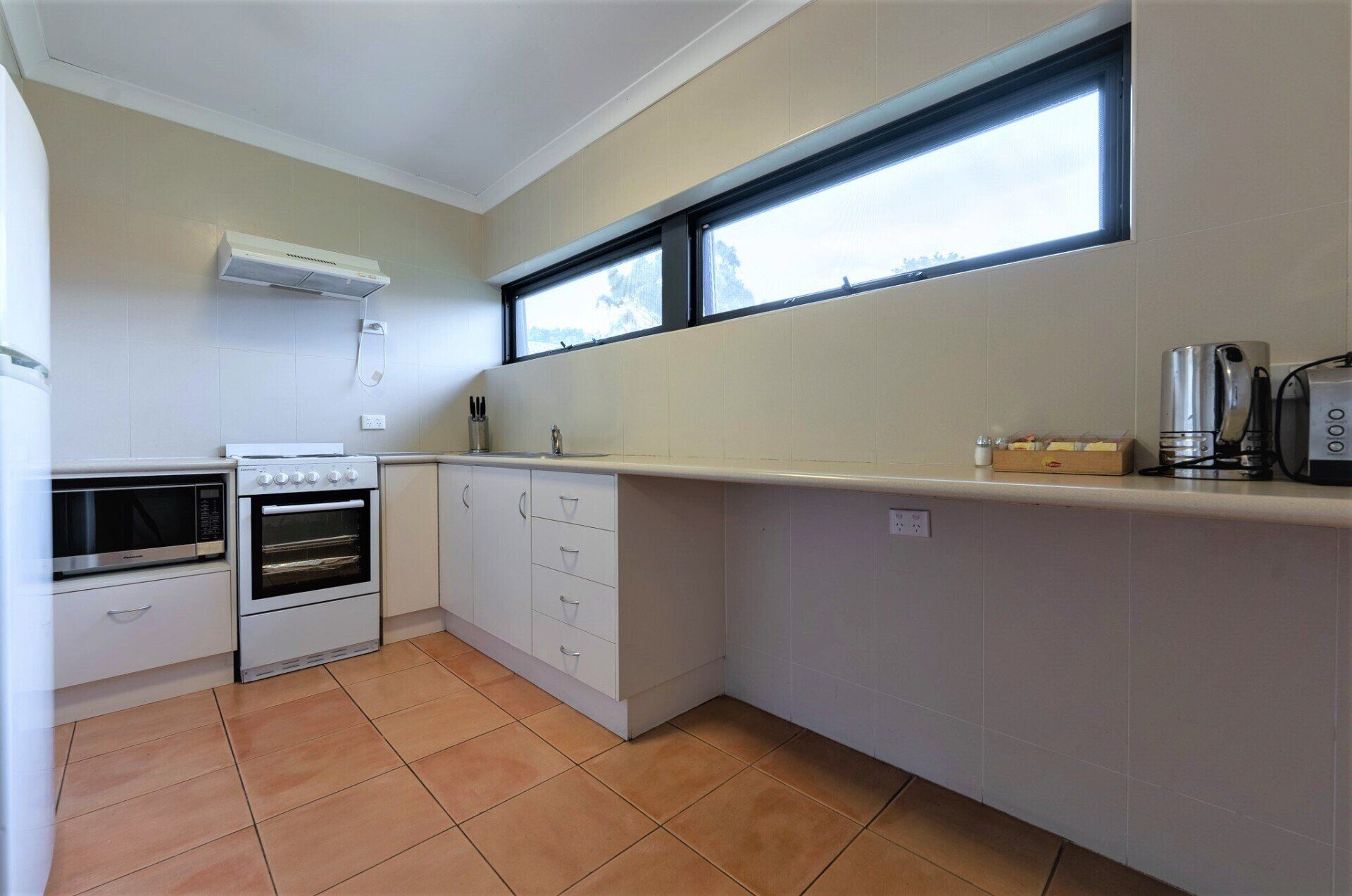 Modern kitchen with terracotta tile floor, white cabinets, long counter, and narrow horizontal windows