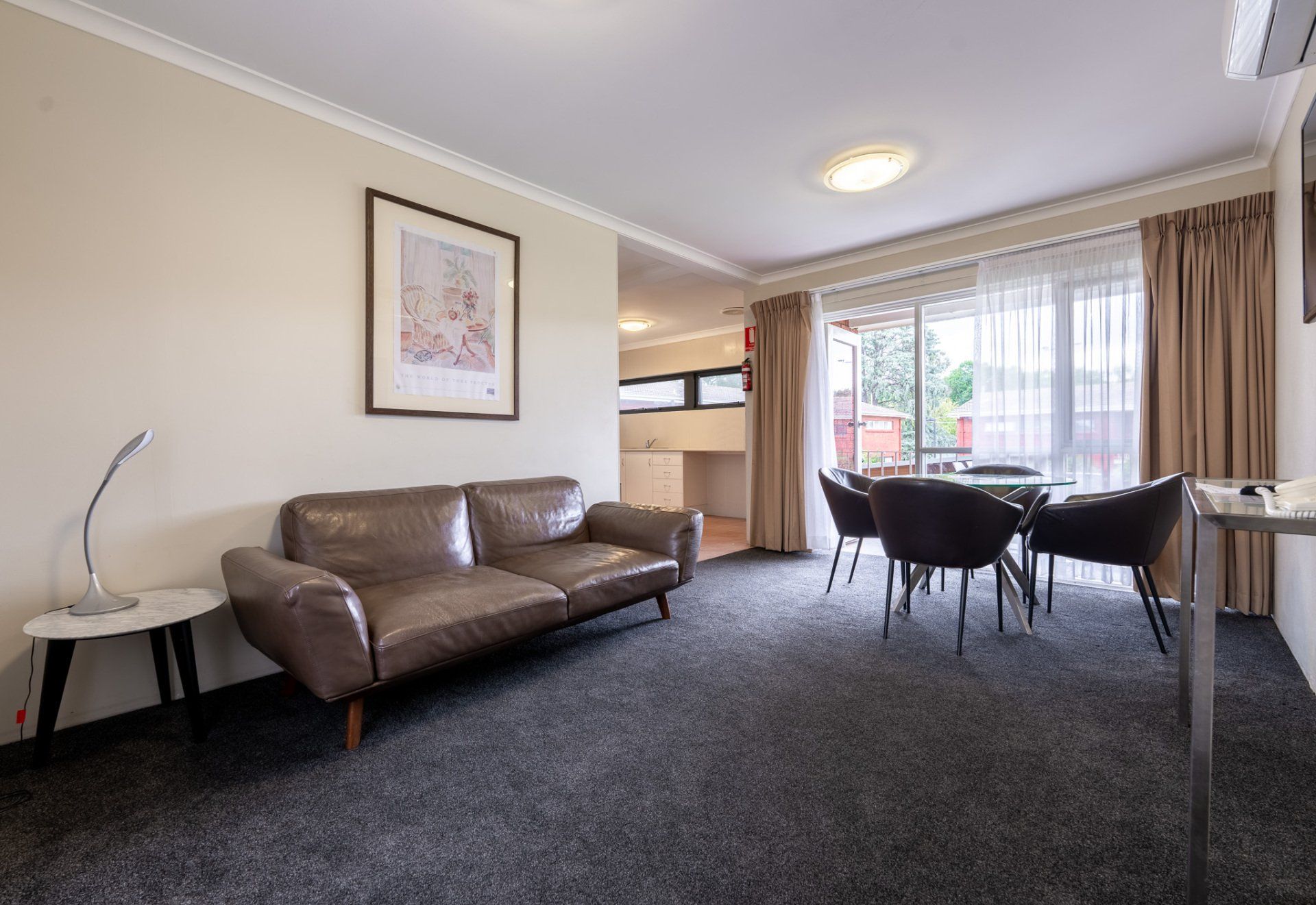 Spacious living room with brown sofa, dining table, carpeted floor, and large windows with curtains