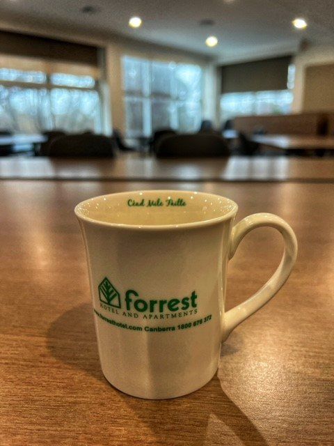 White Forrest coffee mug on a wooden table in a softly lit café.