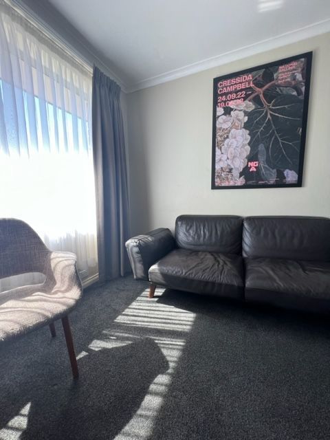 Sunlit living room with black sofa, white chair, and floral wall art by a window with curtains