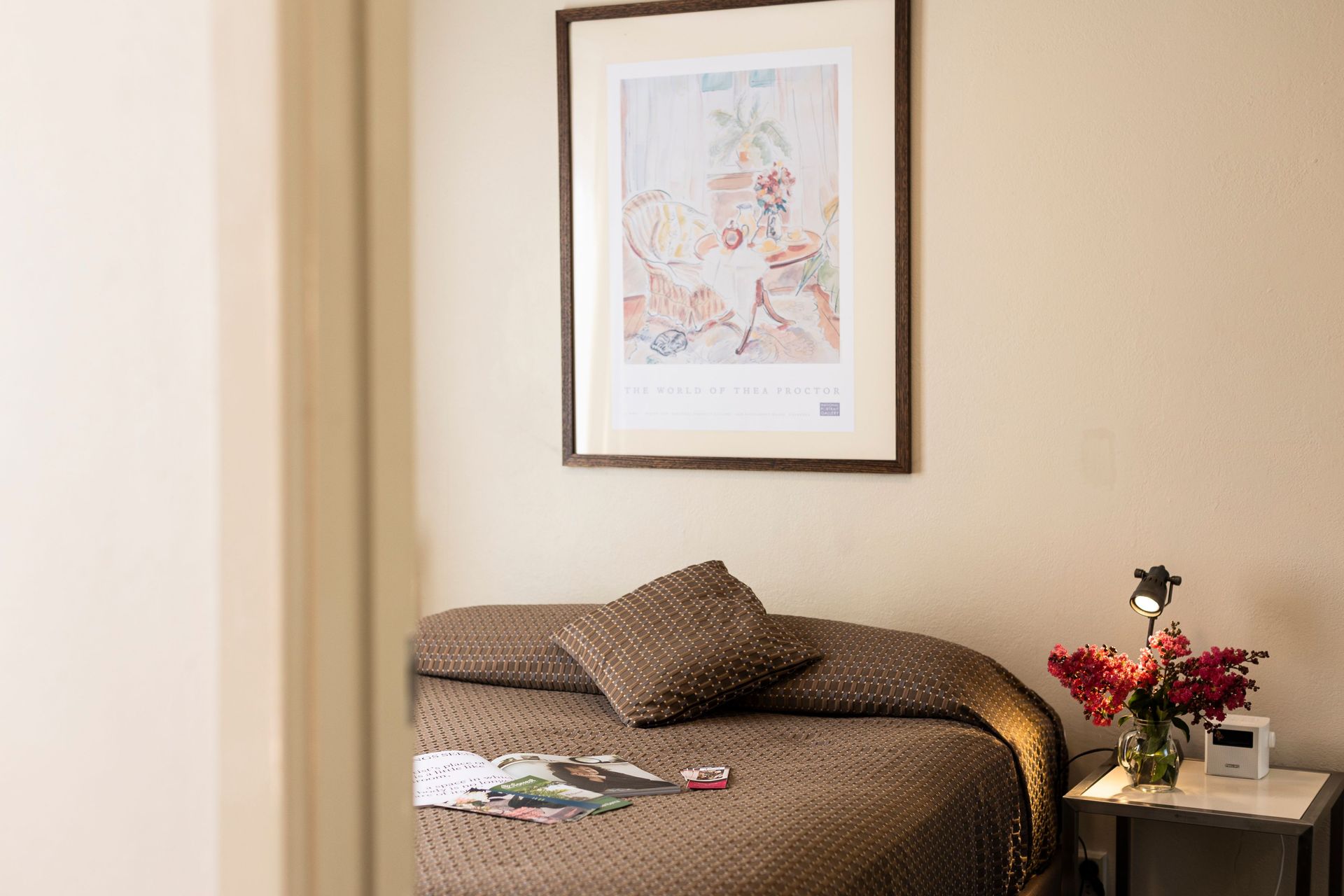 Small bedroom with a bed, framed wall art, and a bedside table holding flowers and a lamp.