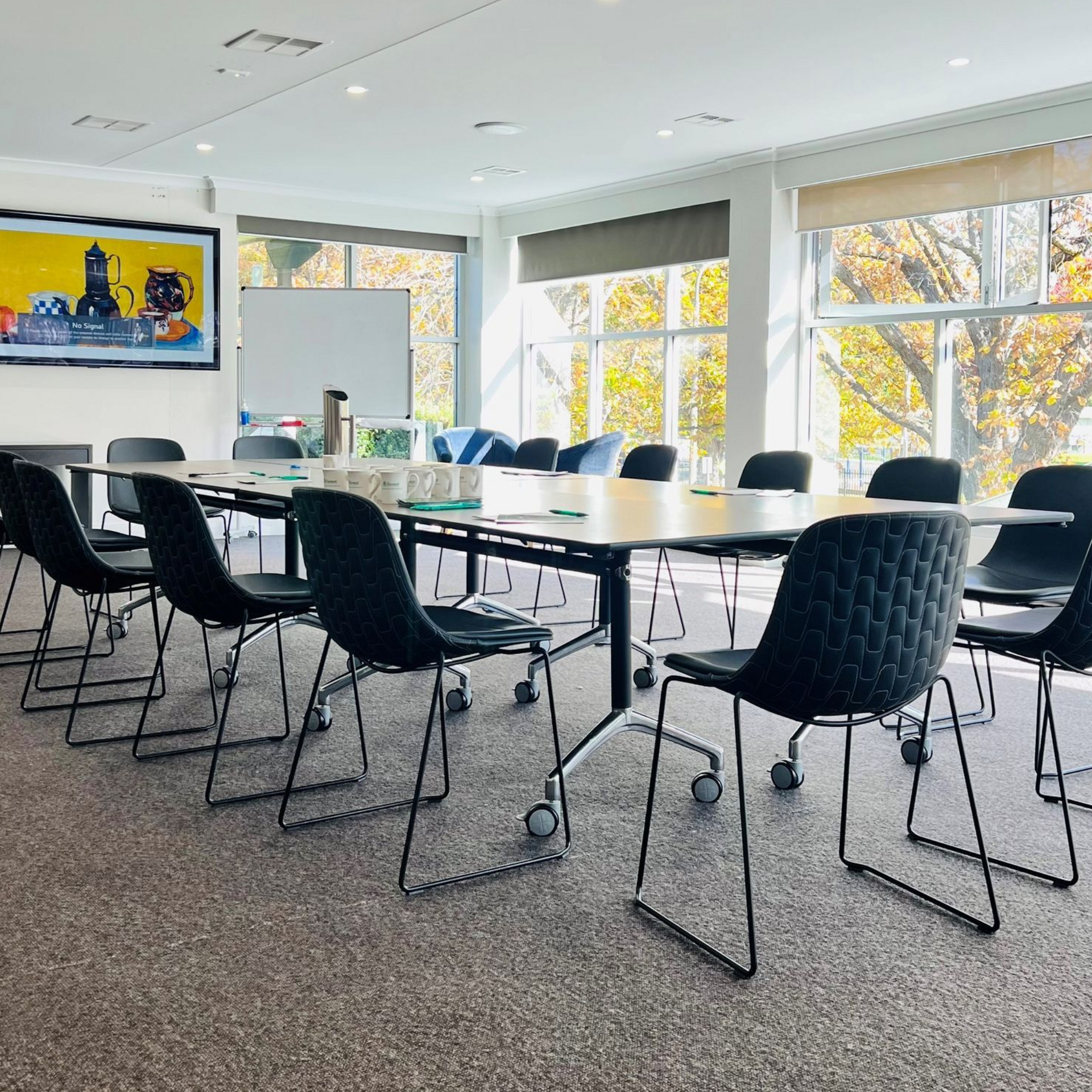 Bright meeting room with black chairs around a long table and large windows letting in autumn light.