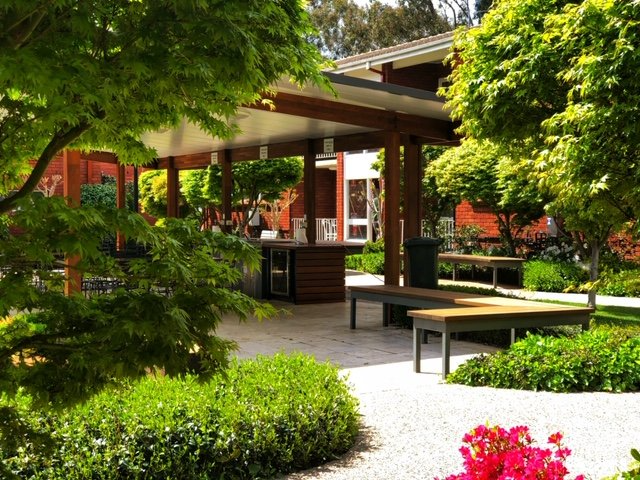 Shaded garden patio with tables, benches, and lush green trees around a pavilion