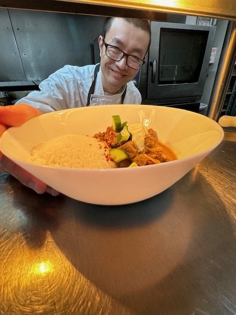 Chef smiling behind a white bowl of pasta in a kitchen