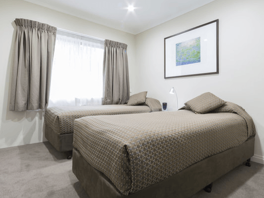 Bright bedroom with two beds, a window with curtains, and a framed picture on the wall