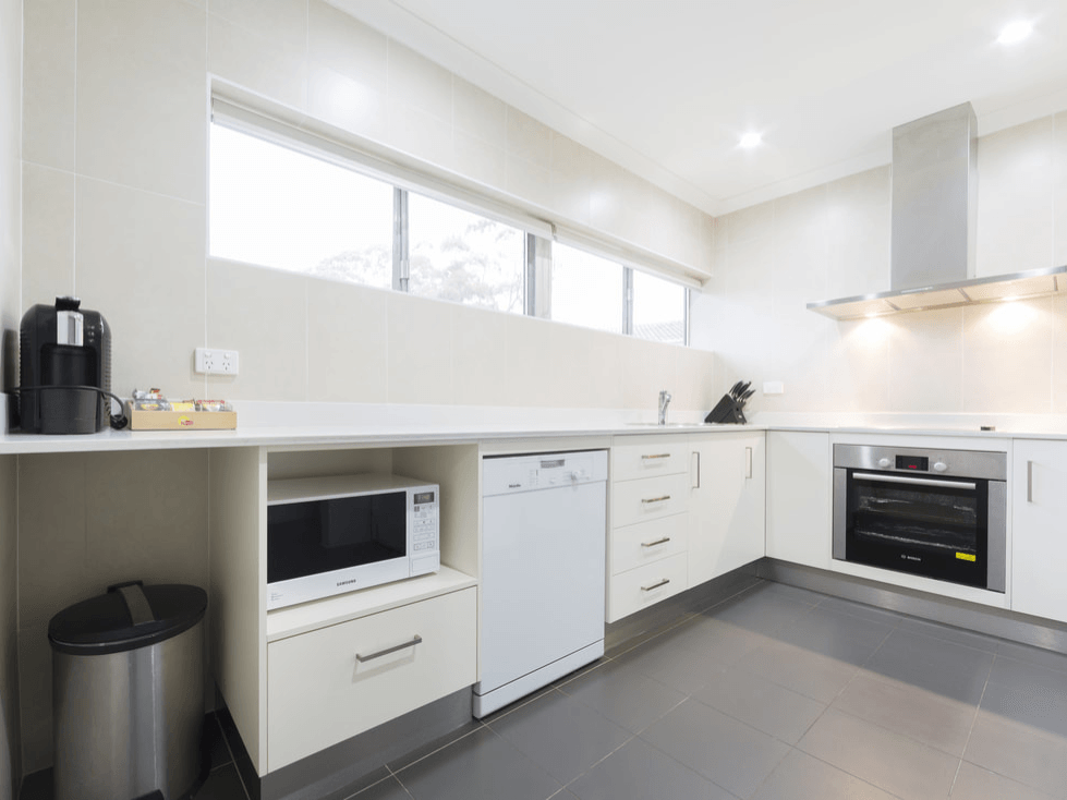 Modern white kitchen with built-in appliances, gray tile floor, and a window over the counter.