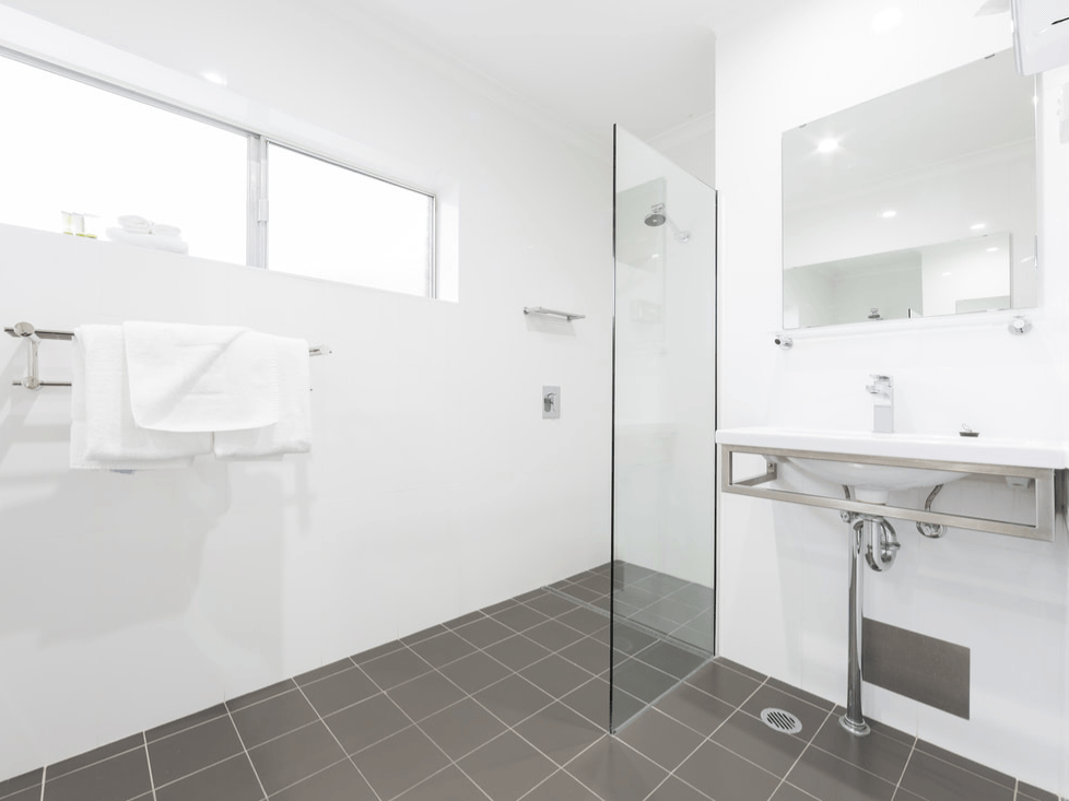 Modern white bathroom with gray tile floor, glass shower, sink, mirror, and towel rack