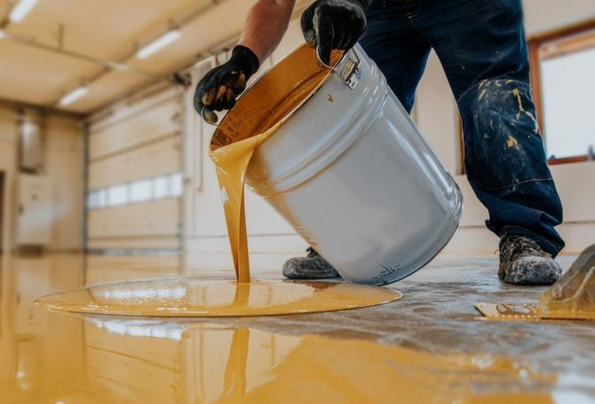 Worker pouring yellow floor coating from a white bucket onto a warehouse floor