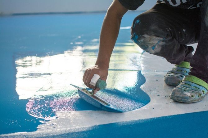 Person kneels painting a glossy blue floor with a roller brush