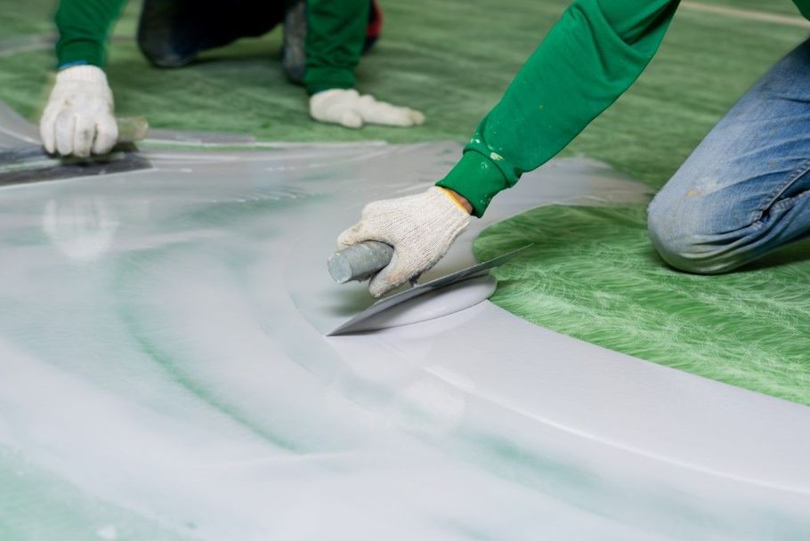 Workers in green gloves smoothing white coating on a green floor surface