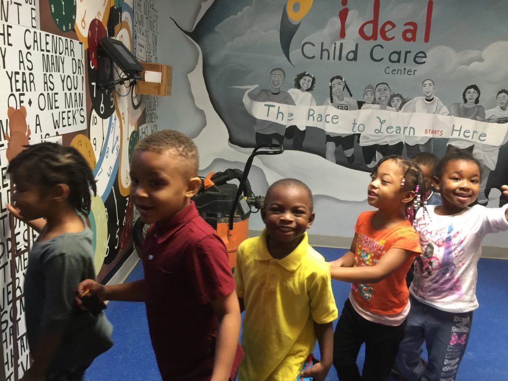 A group of children are standing in front of a wall that says ideal child care