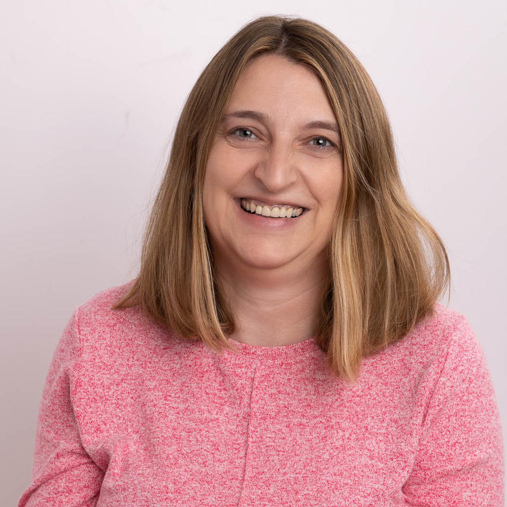 Eine Frau in einem rosa Pullover lächelt in die Kamera.