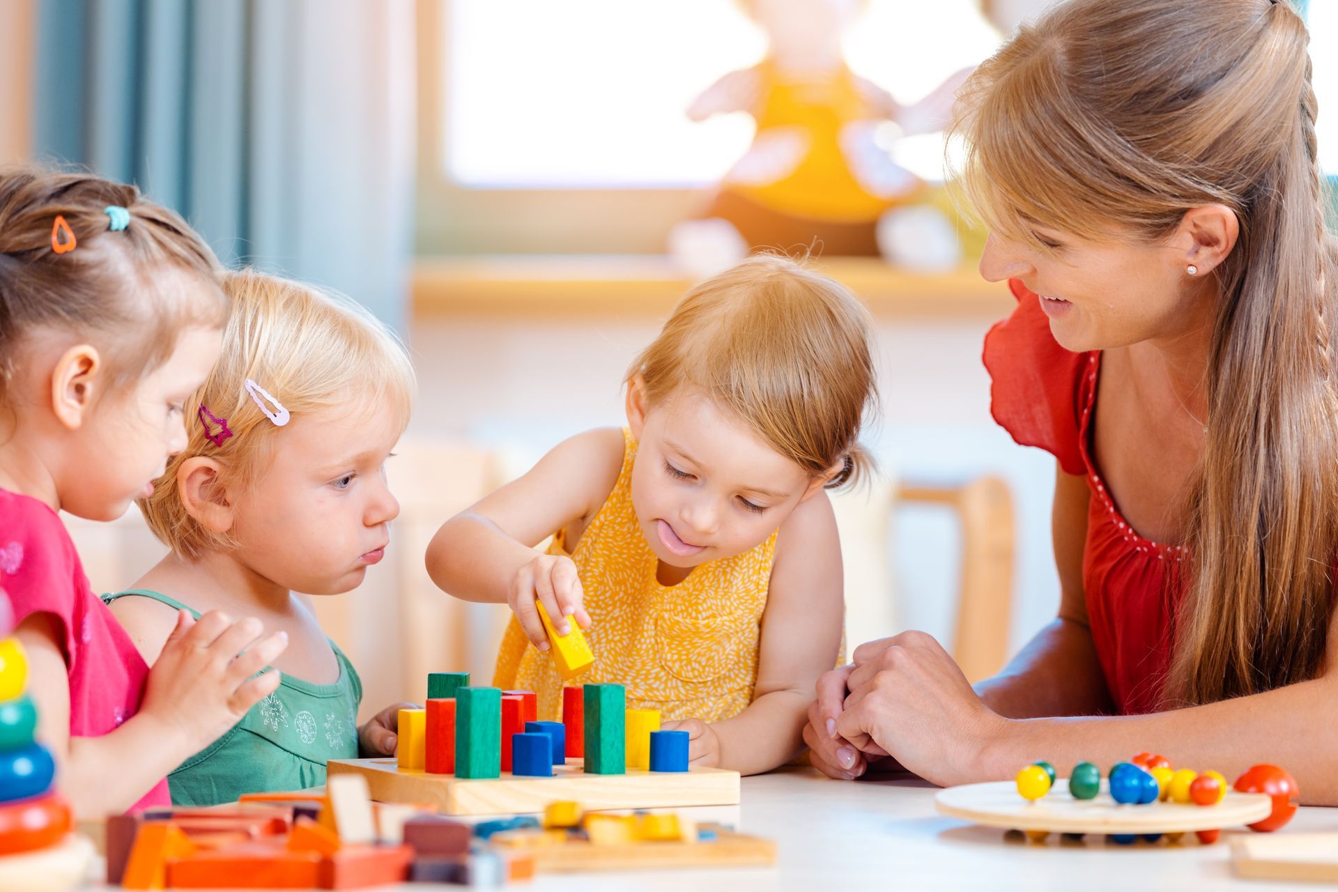 Eine Frau sitzt mit drei kleinen Mädchen an einem Tisch , die mit Spielzeug spielen.