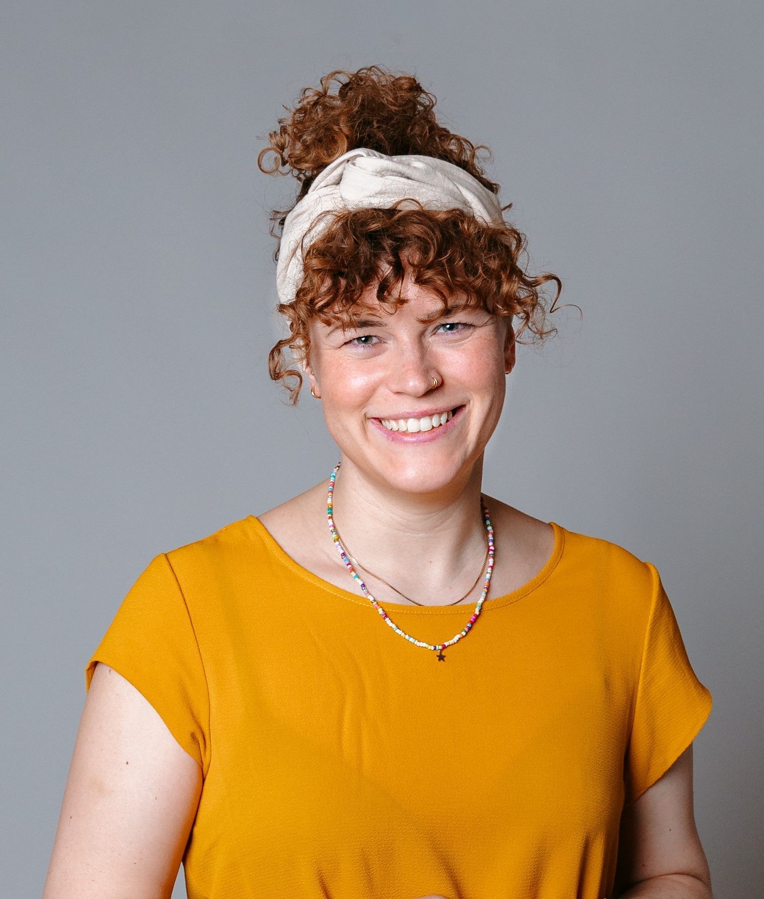 Eine Frau mit lockigem Haar trägt ein gelbes Hemd und ein Stirnband.