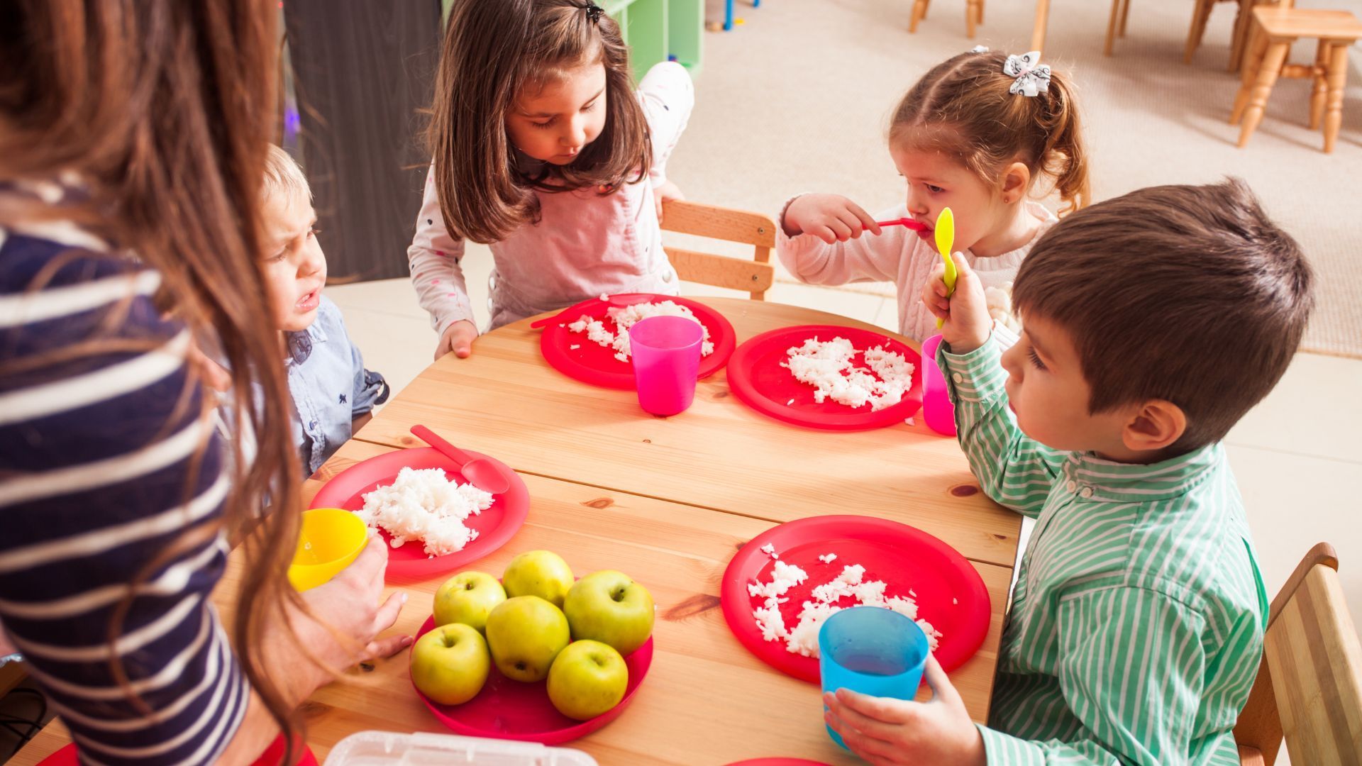 Kinder sitzen an einem Tisch mit roten Tellern und essen zu Mittag