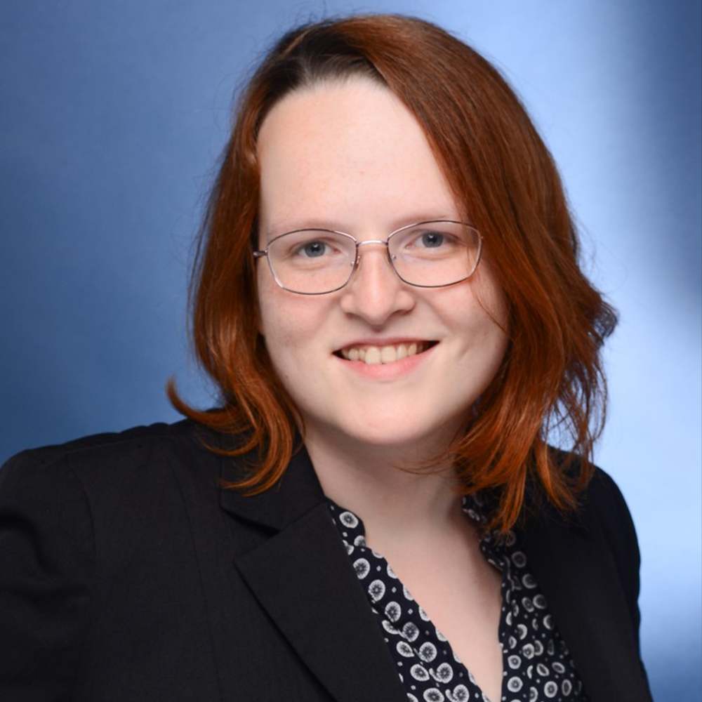 Eine Frau mit roten Haaren, einer Brille und einer schwarzen Jacke