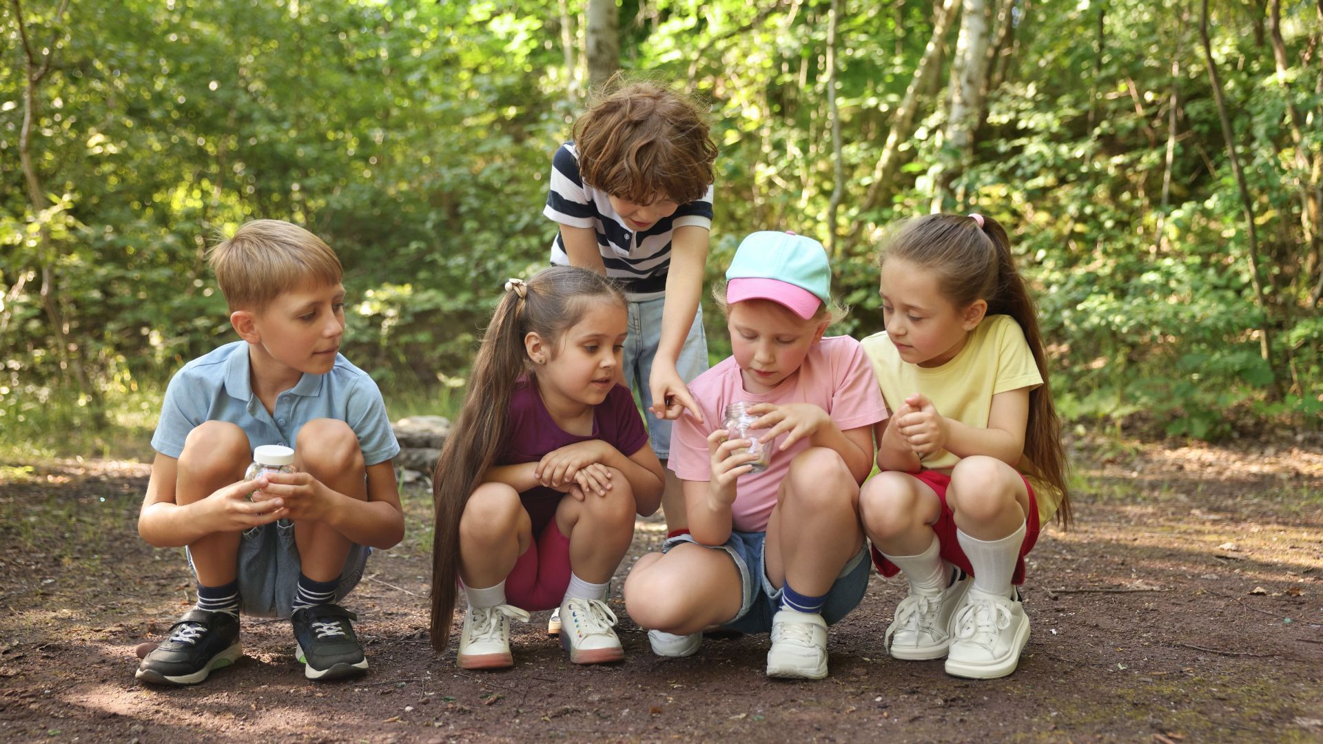 Fünf Kinder hocken auf dem Waldboden und erkunden zusammen etwas, dass sie gefunden haben.