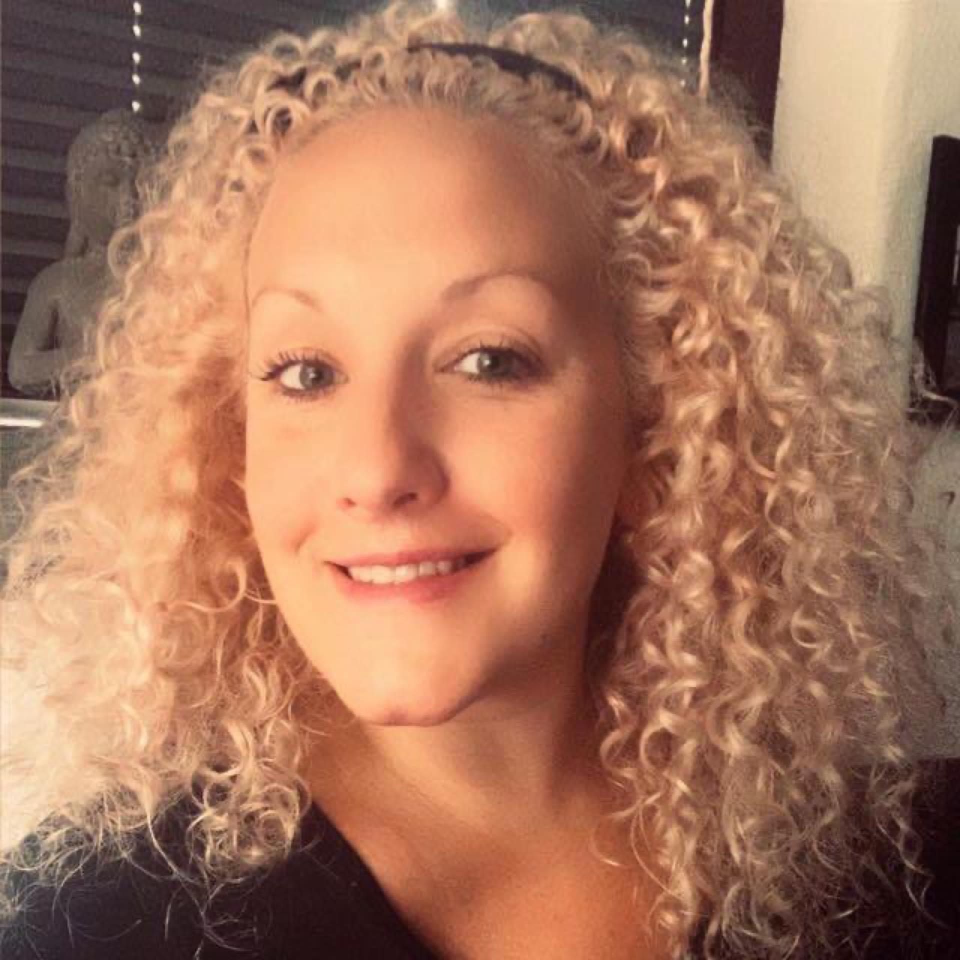 Eine Frau mit blonden Locken lächelt in die Kamera.