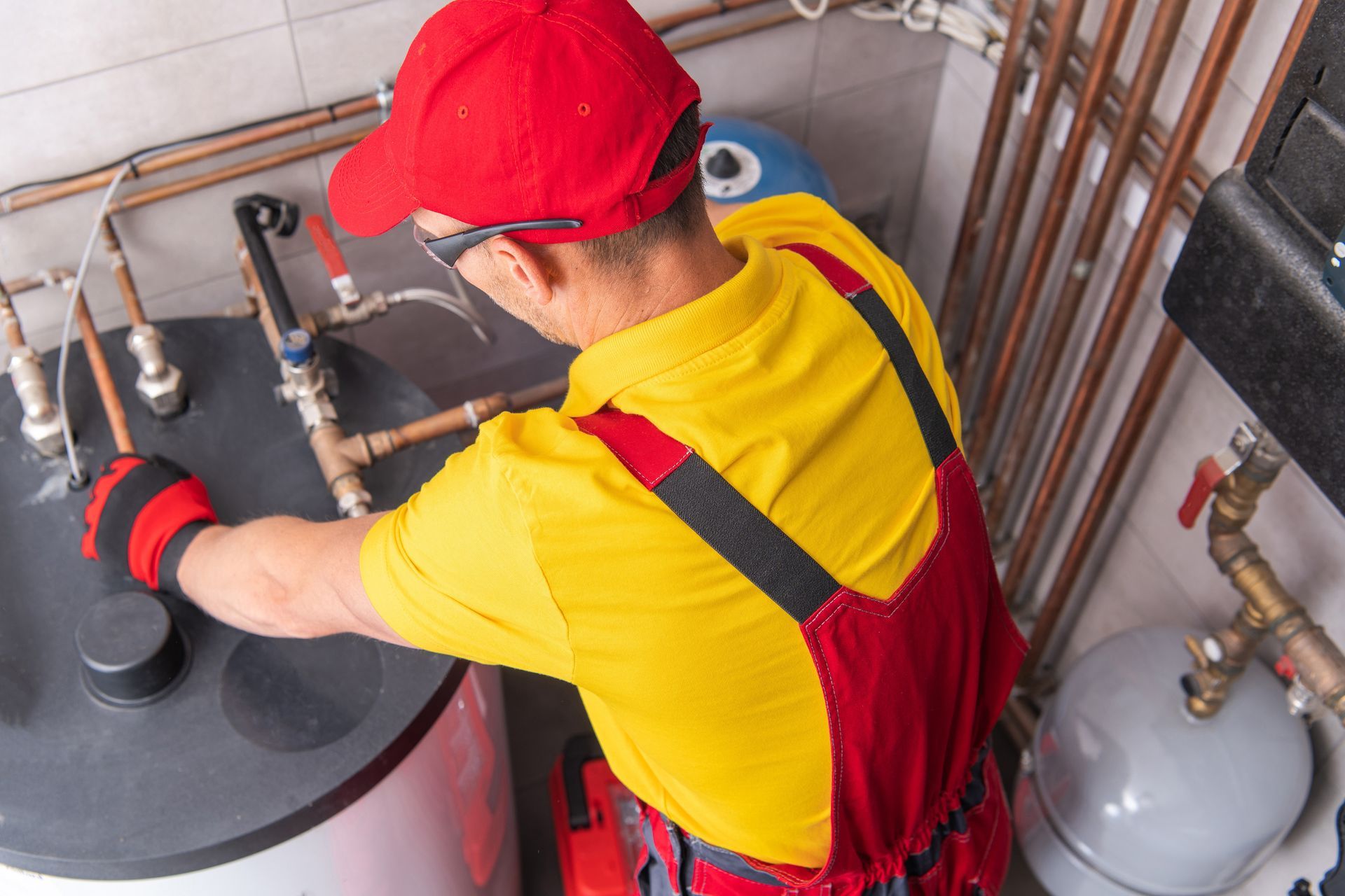 A plumber adjusting pipes and valves on a water heater system in a utility room