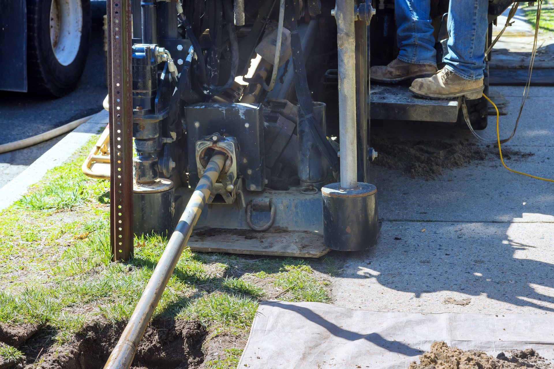 Directional drilling machine operating on grass near pavement with drill pipe entering the ground.