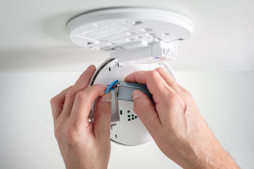 Hands wiring a white ceiling smoke detector during installation