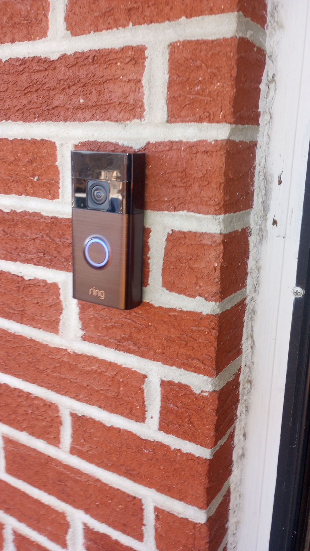 Video doorbell on a red brick wall beside a door frame.