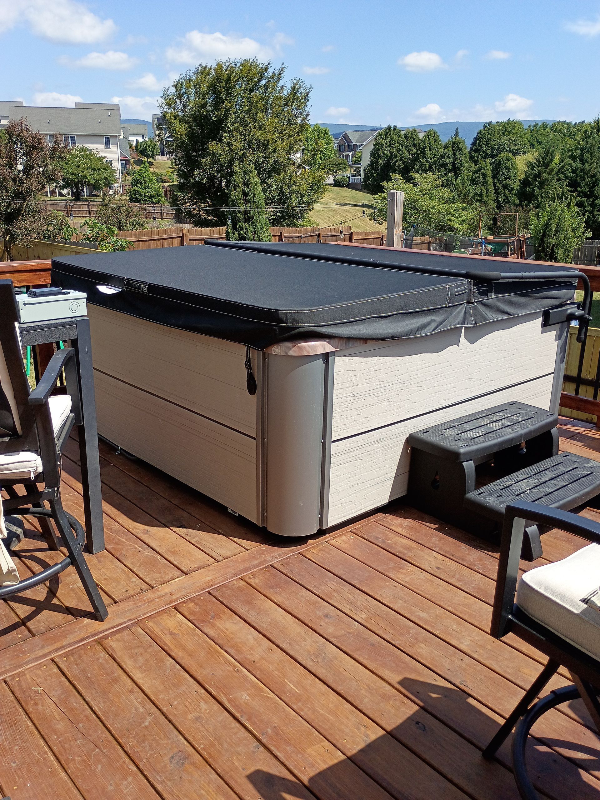 Outdoor patio with a covered hot tub, wooden deck, and surrounding chairs under sunny skies