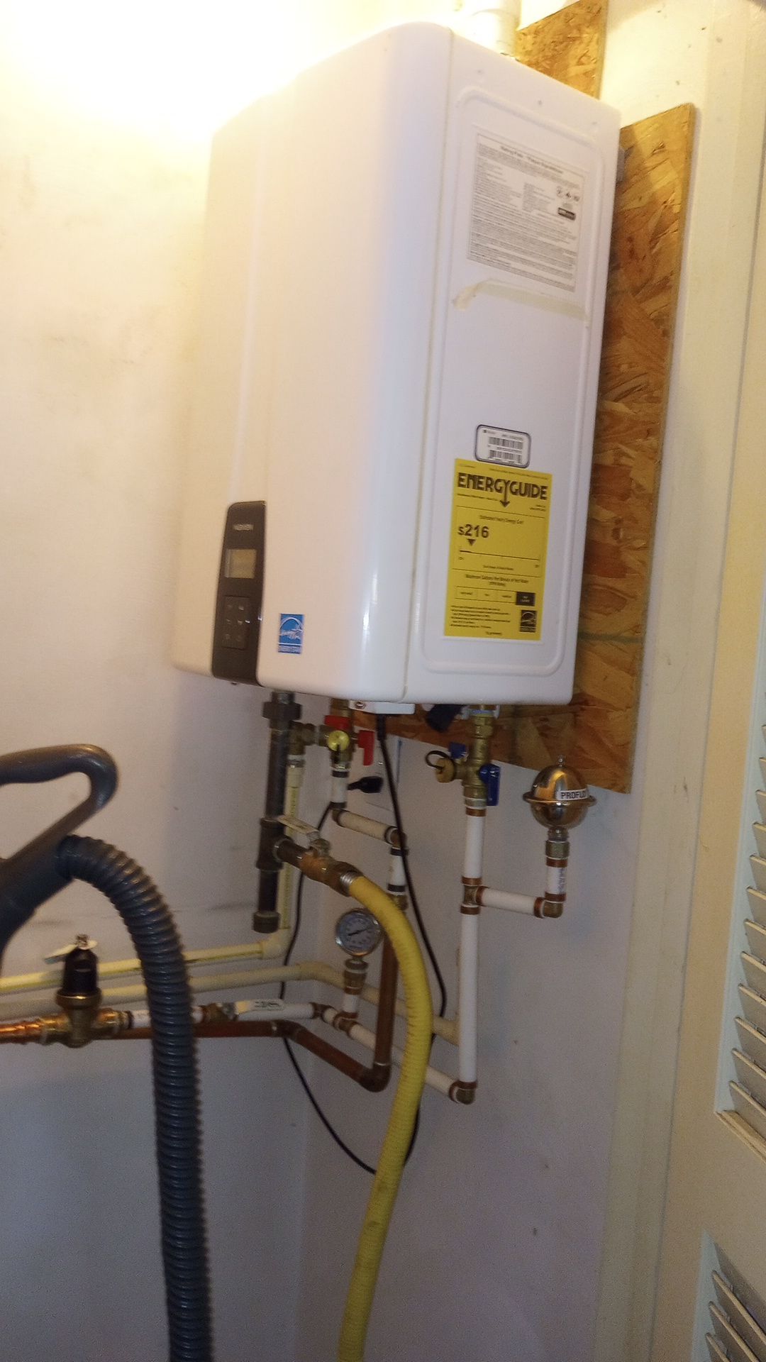 Wall-mounted white water heater with pipes and hoses in a utility closet.