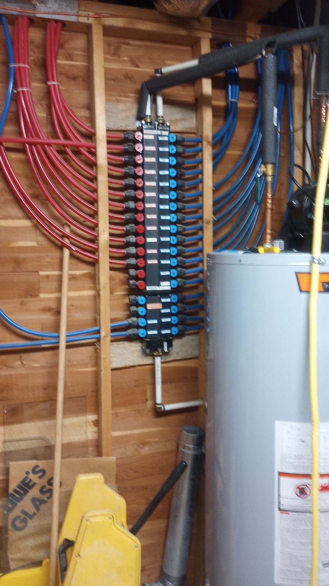 Water heater and electrical panel with red and blue wiring in an unfinished basement.