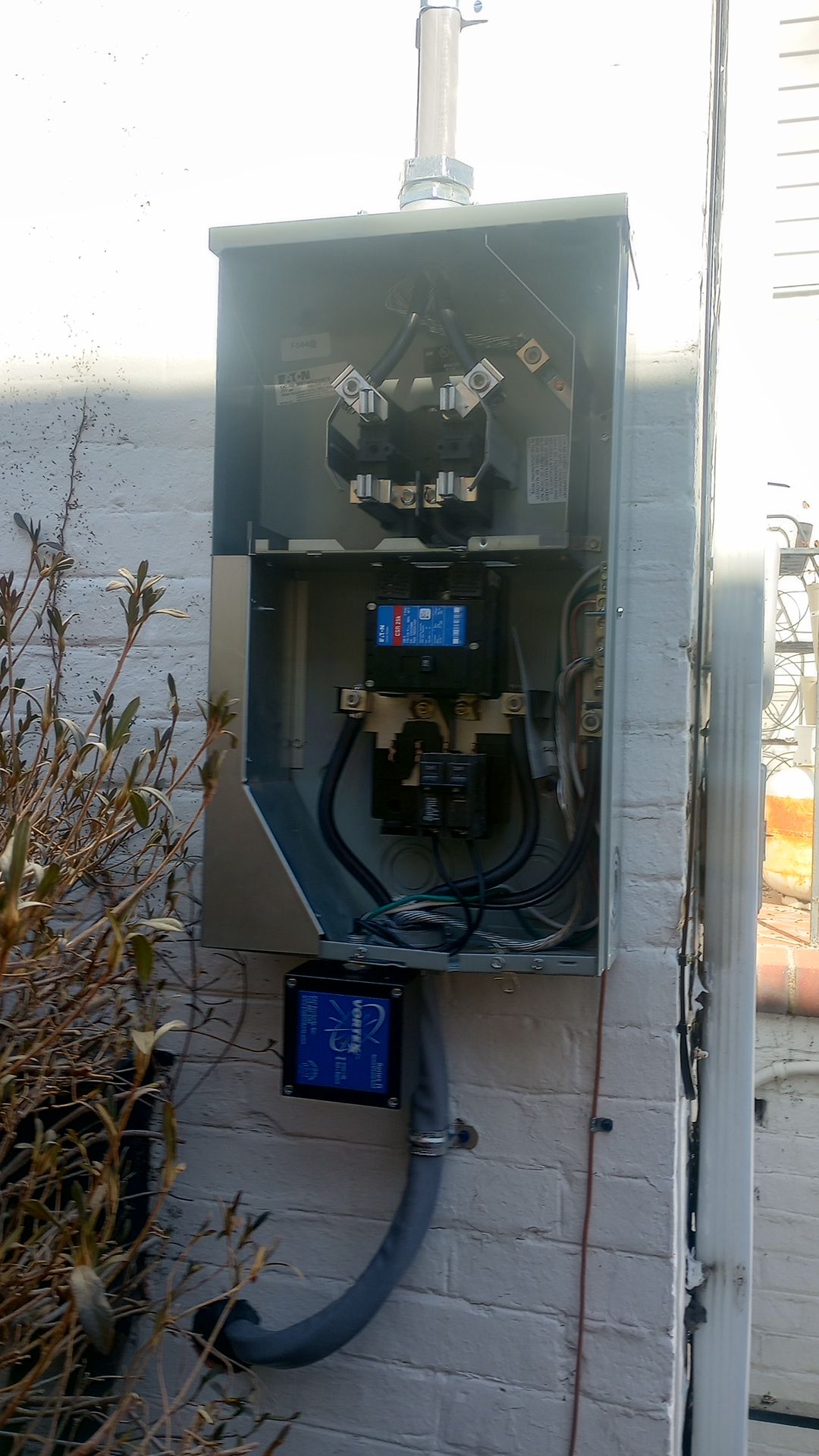 Open electrical meter box mounted on a brick wall with visible wiring and conduit