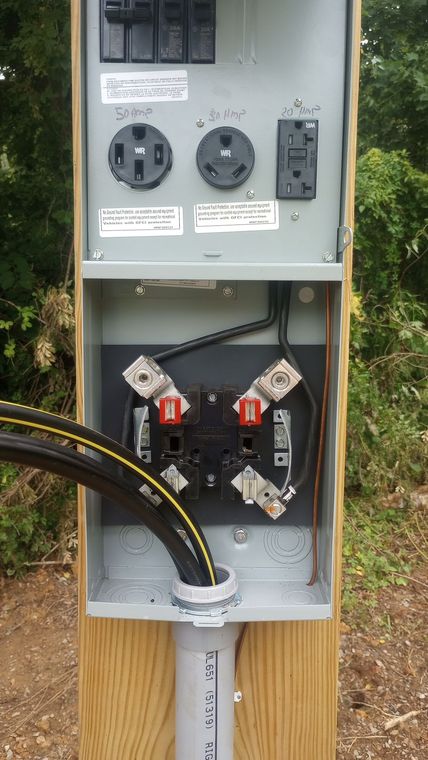 Open electrical service panel with outlets and meter sockets on a wooden post outdoors