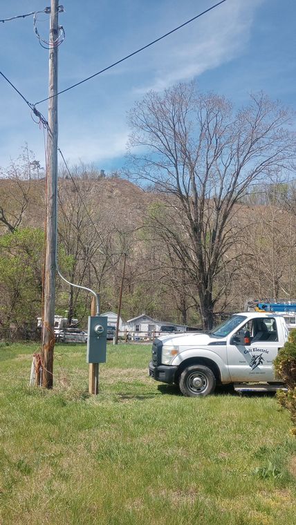 Utility truck parked in a grassy roadside area near a utility pole and trees on a sunny day