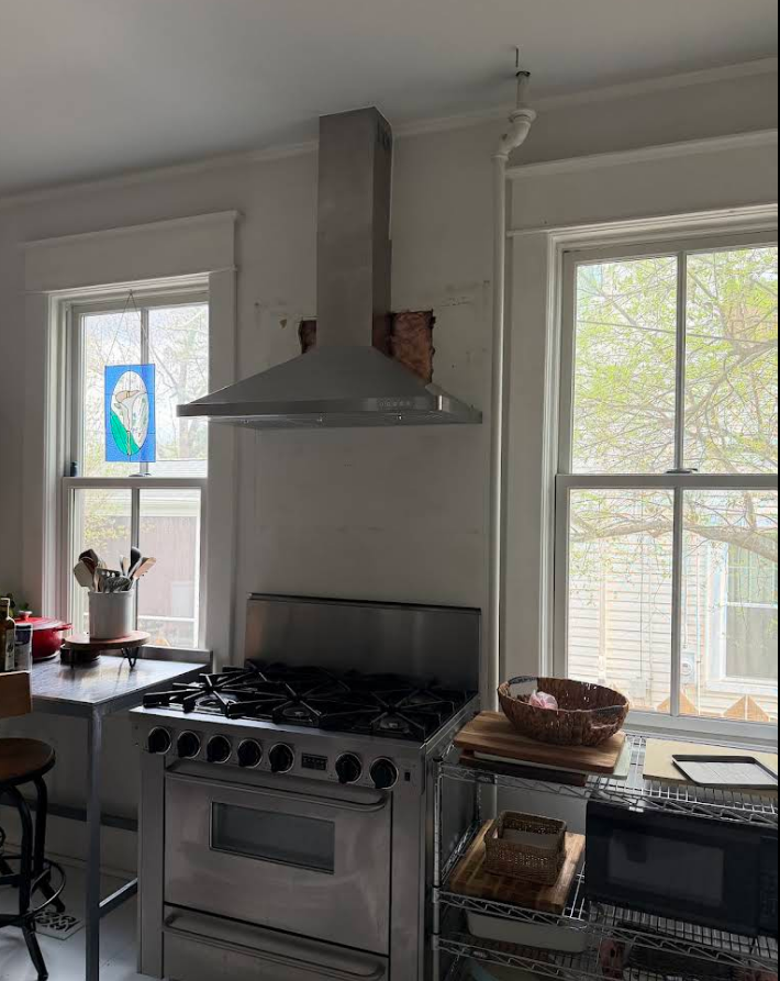 Modern kitchen with stainless steel stove, vent hood, and two windows with a colorful stained-glass panel.