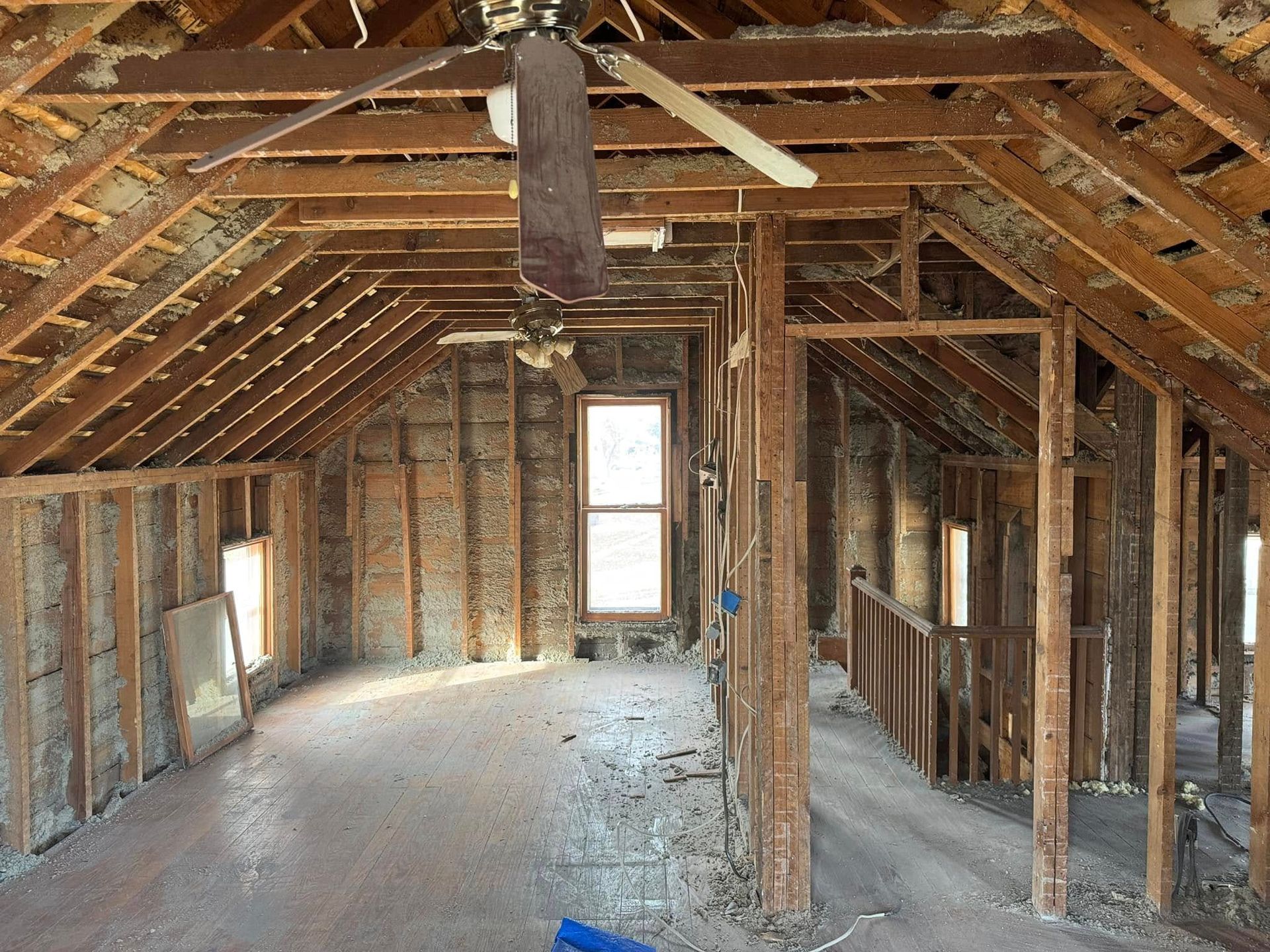 Interior of an unfinished attic space with exposed wooden beams, insulation, and windows.
