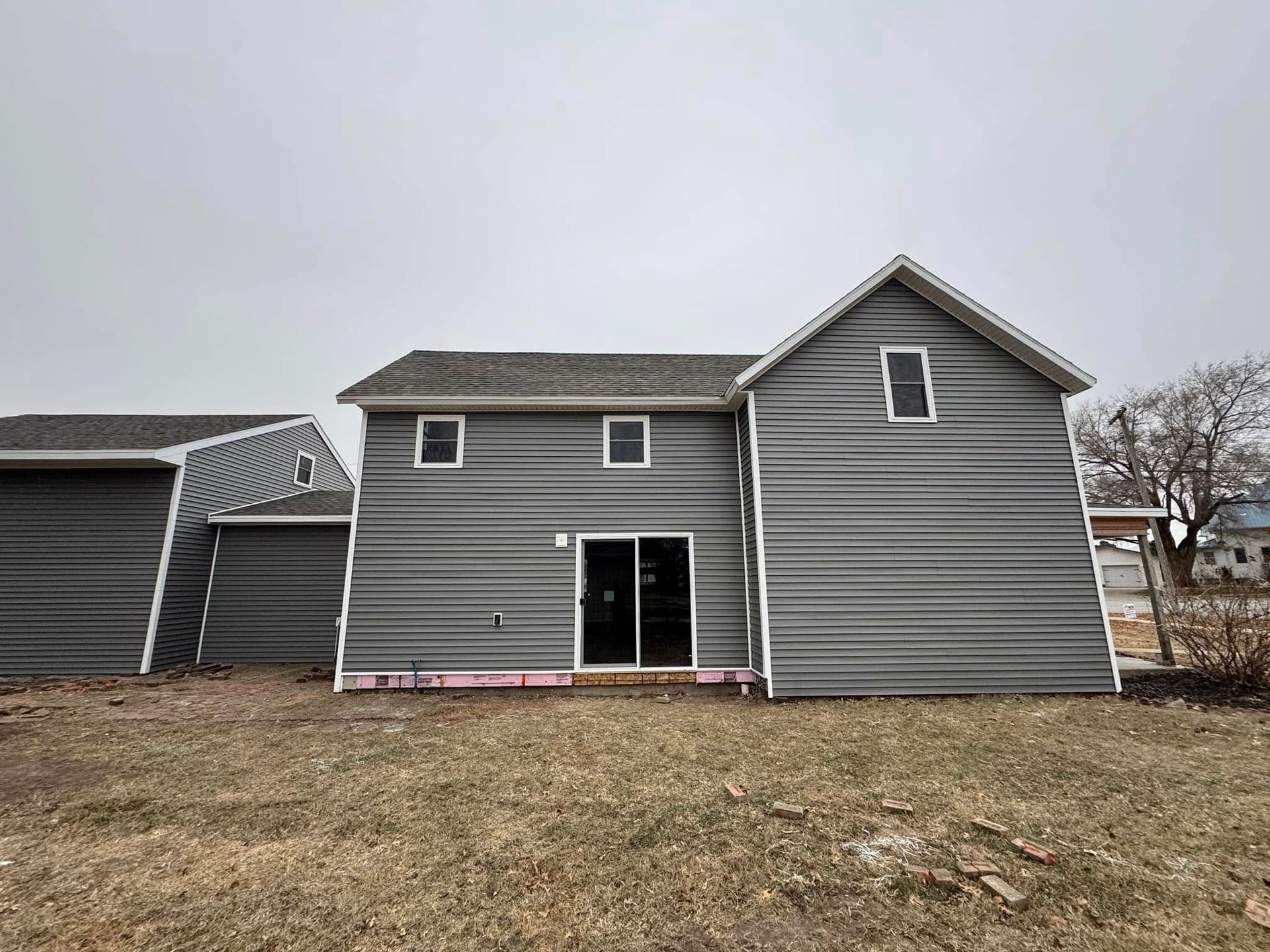 Gray-sided house with a gable roof, two levels, and a sliding glass door. Overcast sky.
