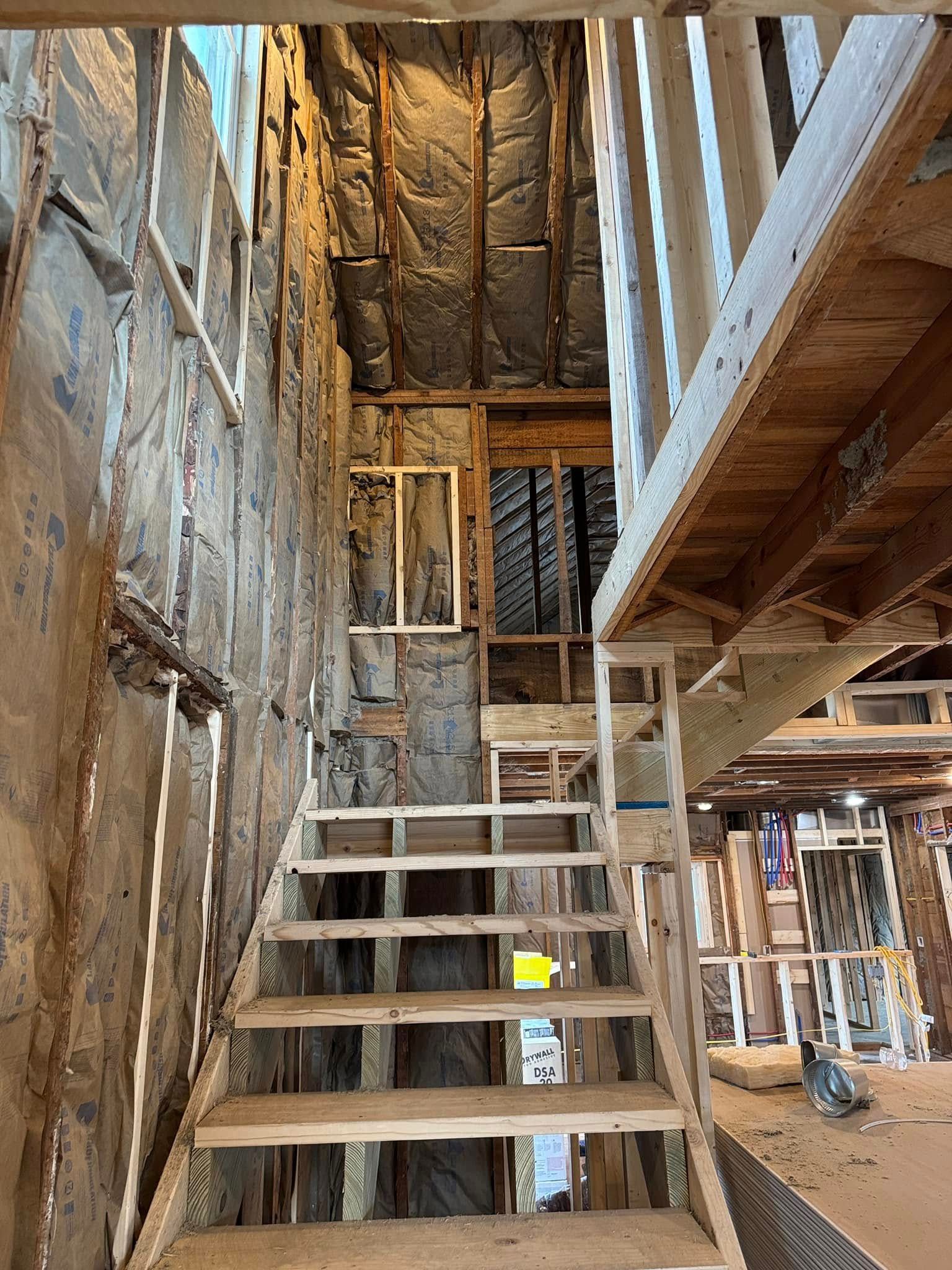 Staircase under construction with exposed framing and insulation, leading to an upper level.