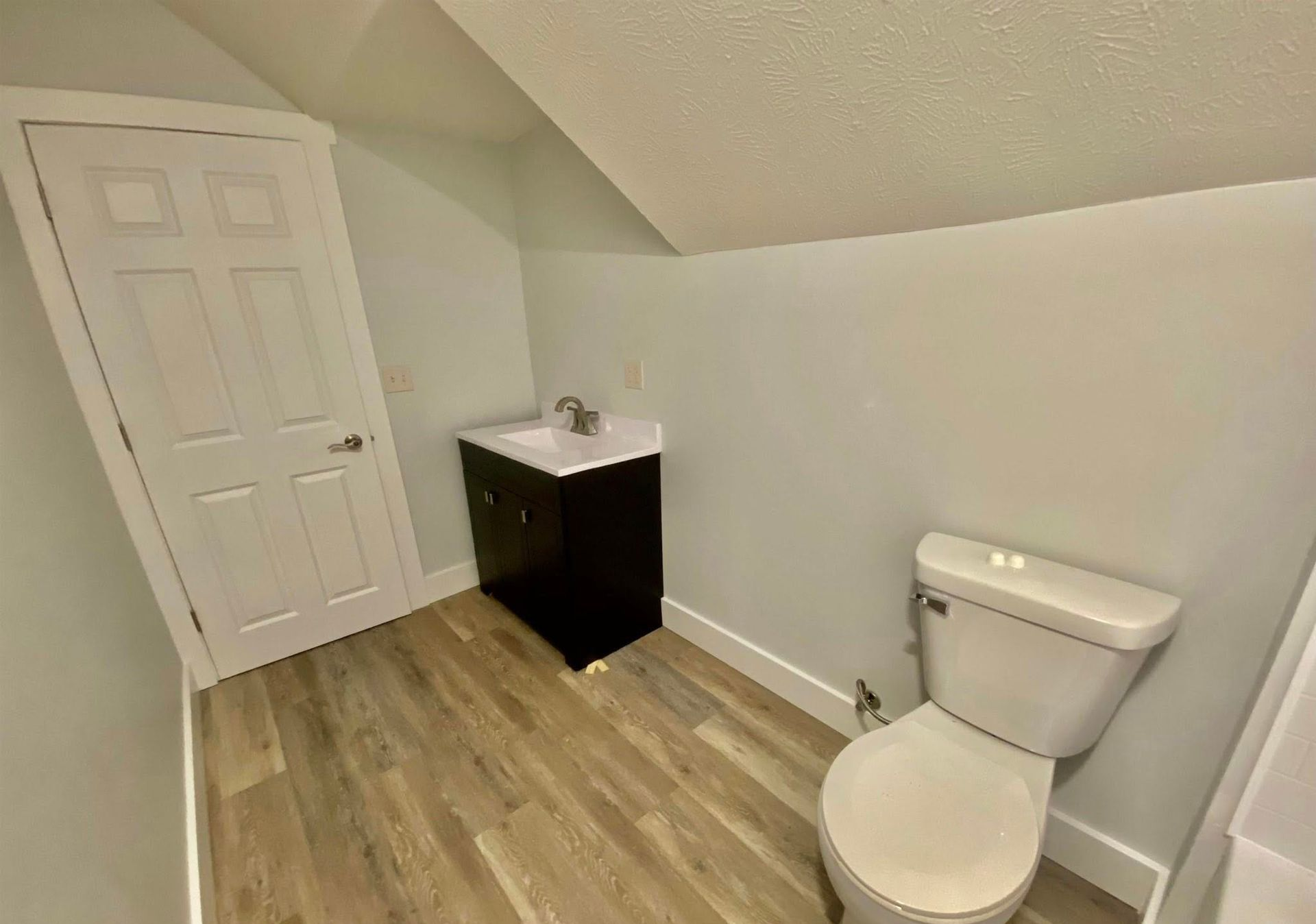Small bathroom with a toilet, vanity, and closed door under sloped ceiling.