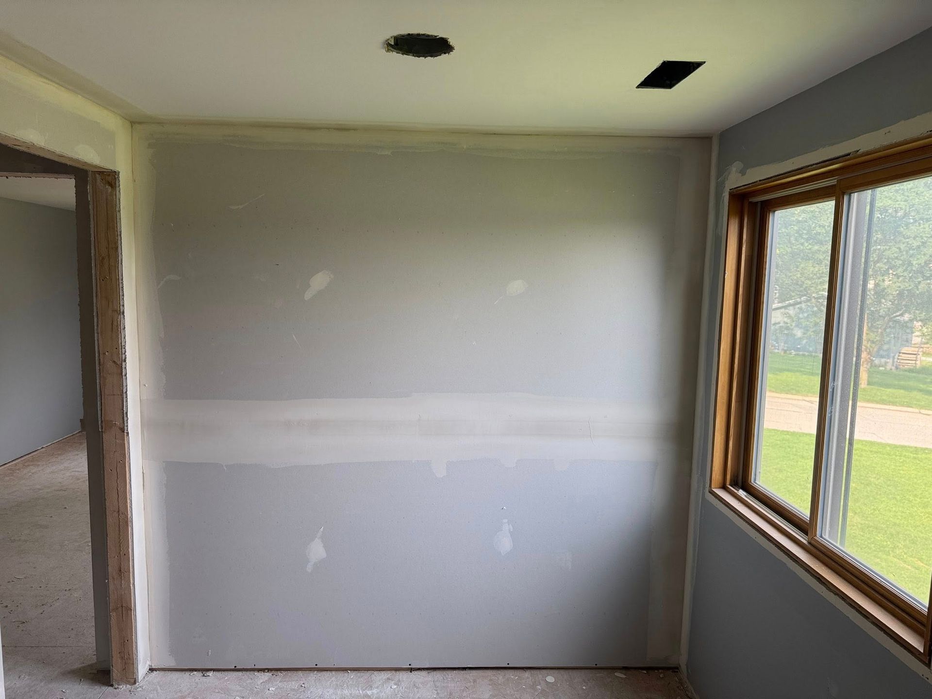 Interior wall with drywall, window, and door frame. Gray walls, unfinished.