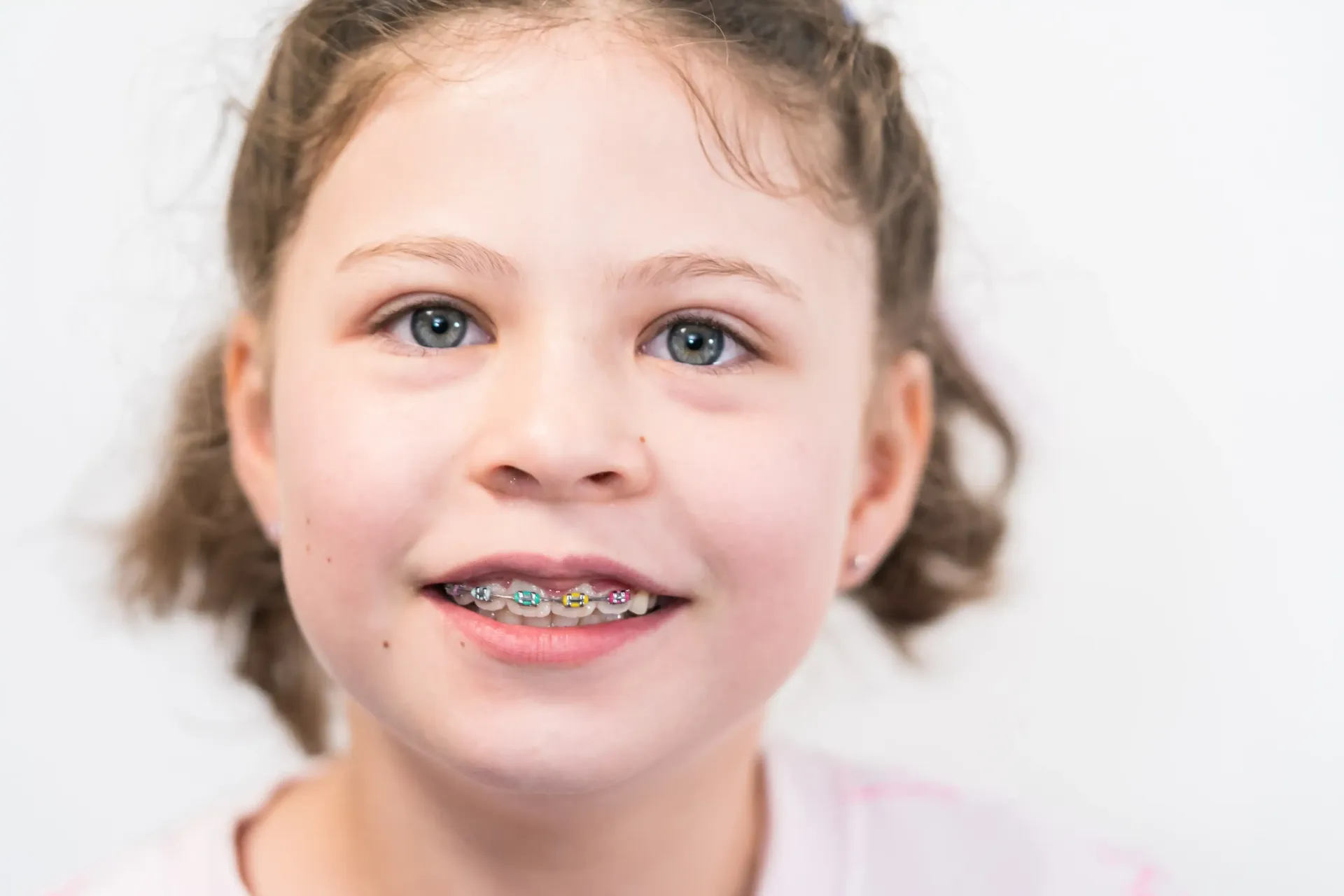 Close-up portrait of a young girl smiling with colorful braces.