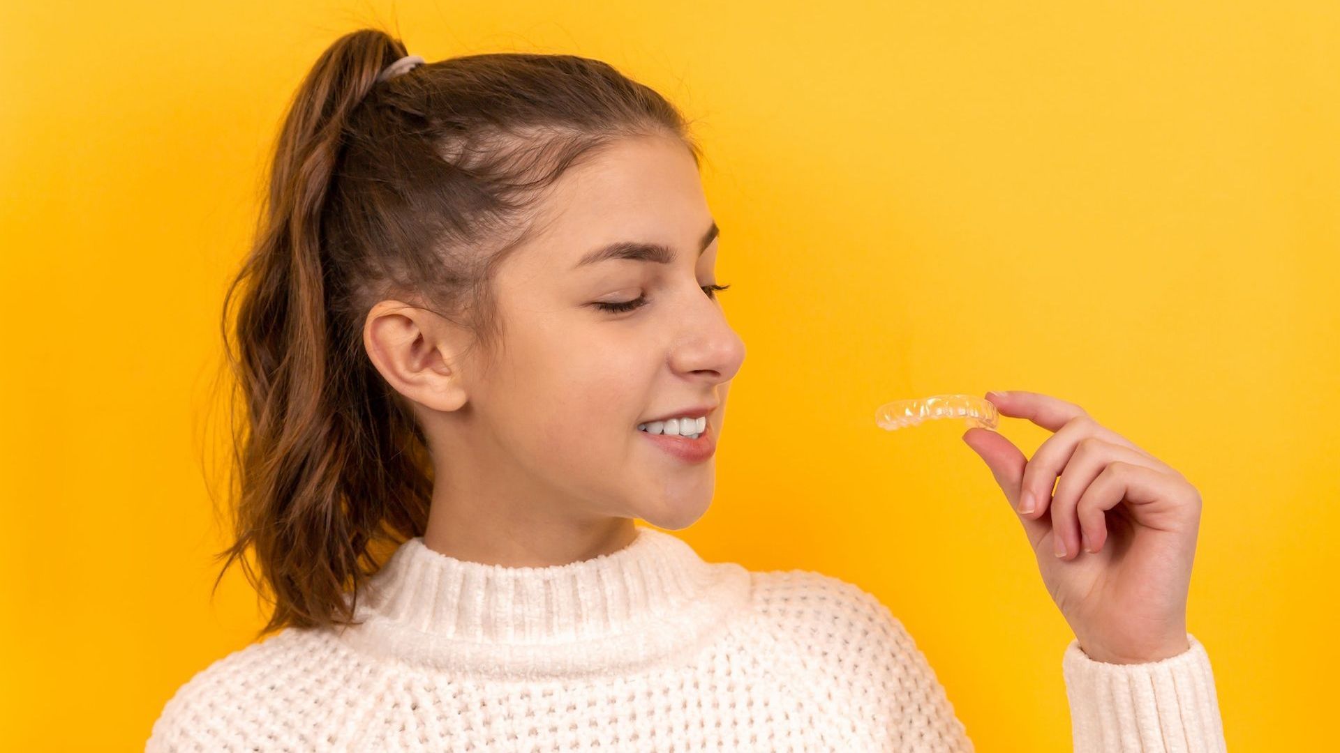 a woman in a white sweater is holding a clear retainer in her hand
