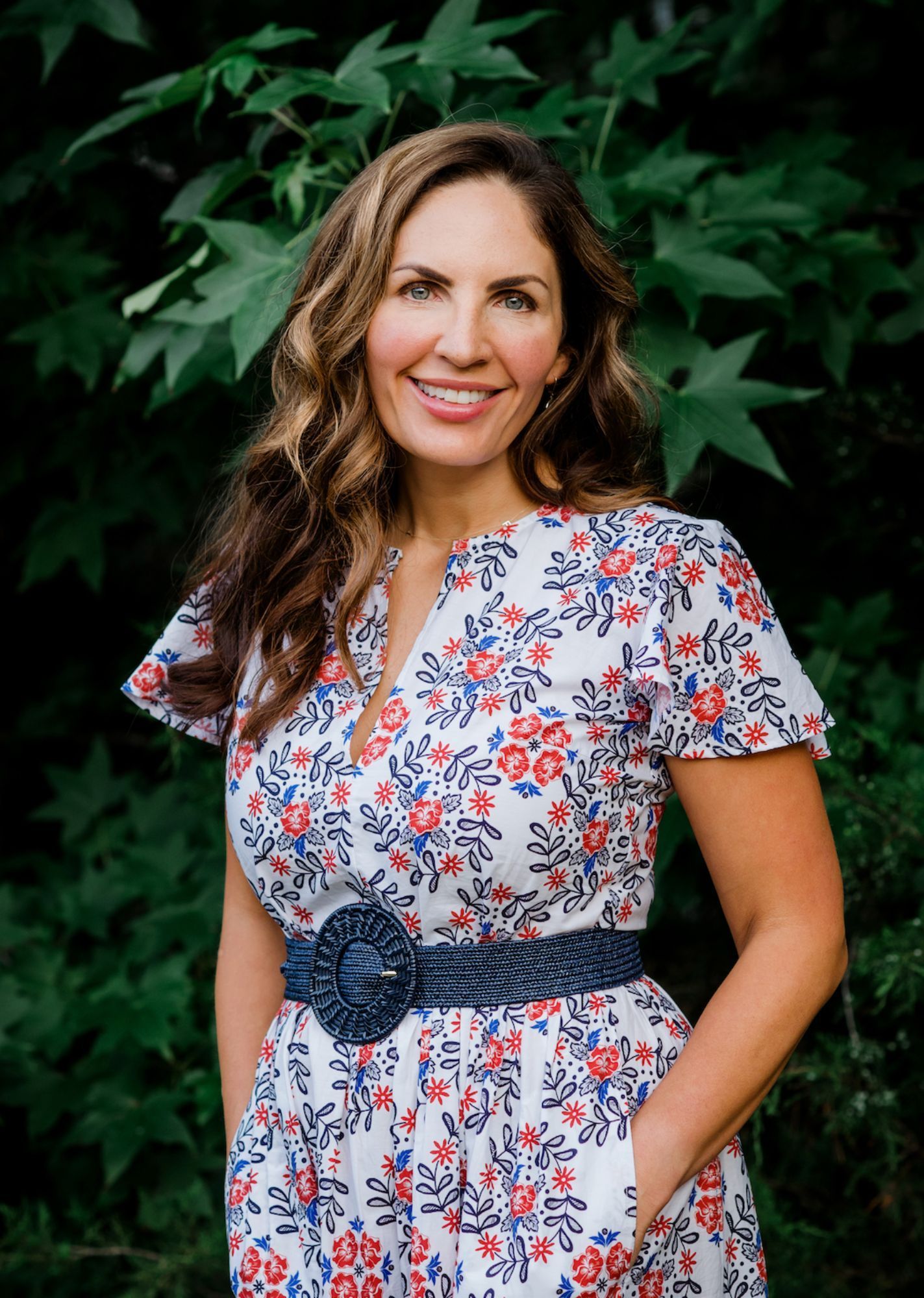 Dr. Sarah is smiling and posing in front of green leaves.