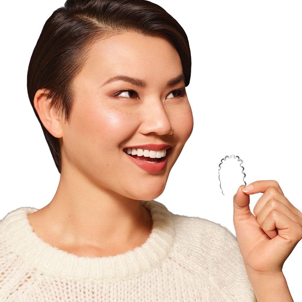 Smiling woman holding a custom lingual orthodontic wire.