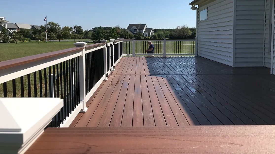 A wooden deck with a white railing and a white house in the background
