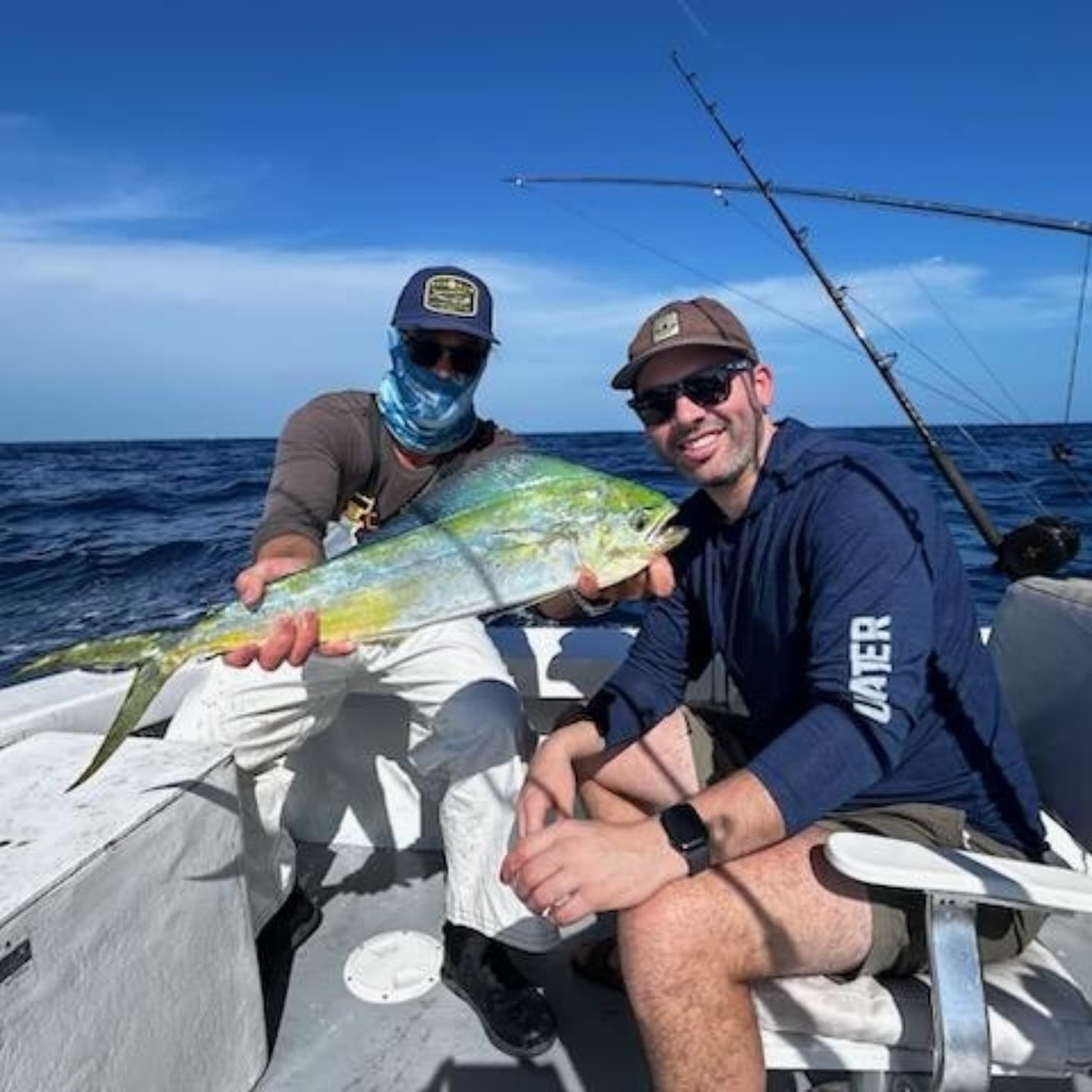 Two people on a boat holding a mahi-mahi fish under a clear blue sky.