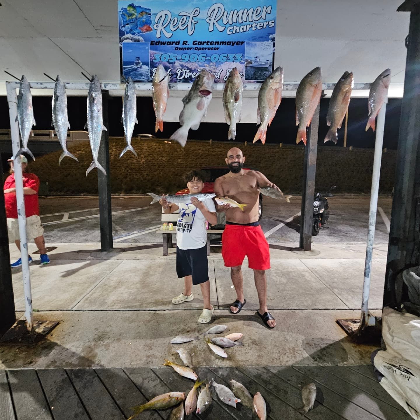 Two people hold fish in front of a rack of hanging catches at a 
