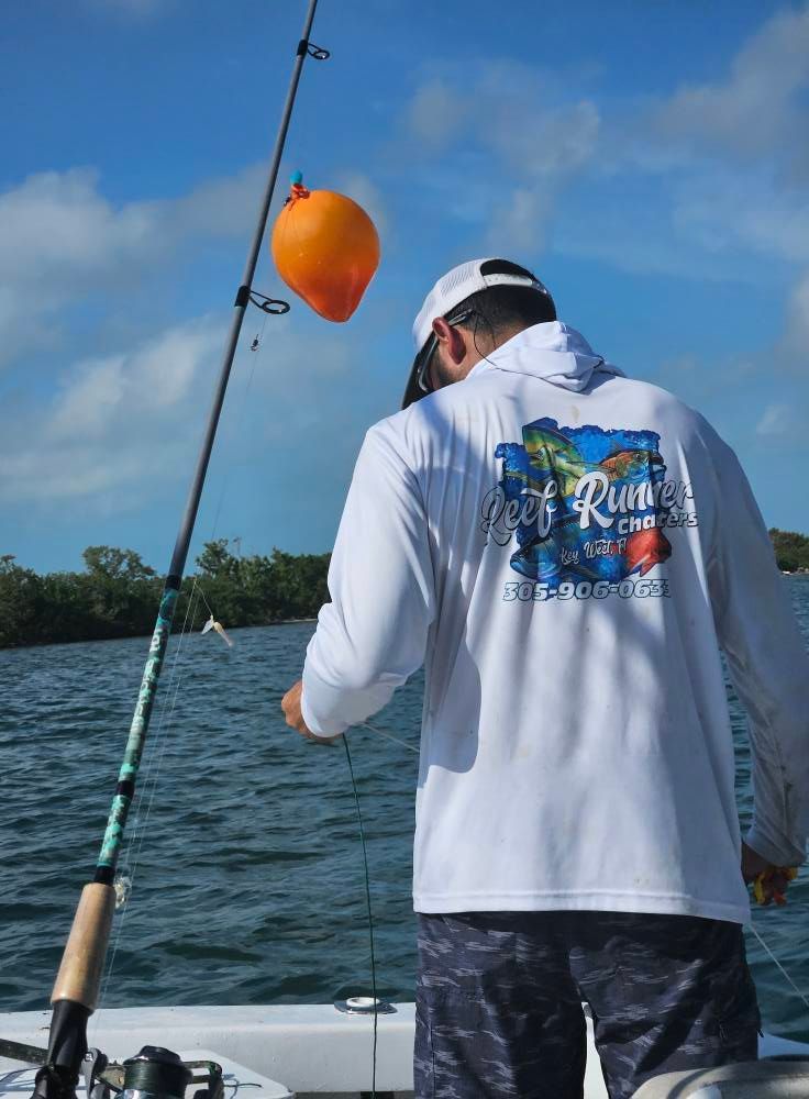 A person in a white long-sleeve shirt stands on a boat, holding a fishing line attached to a bright orange balloon float.