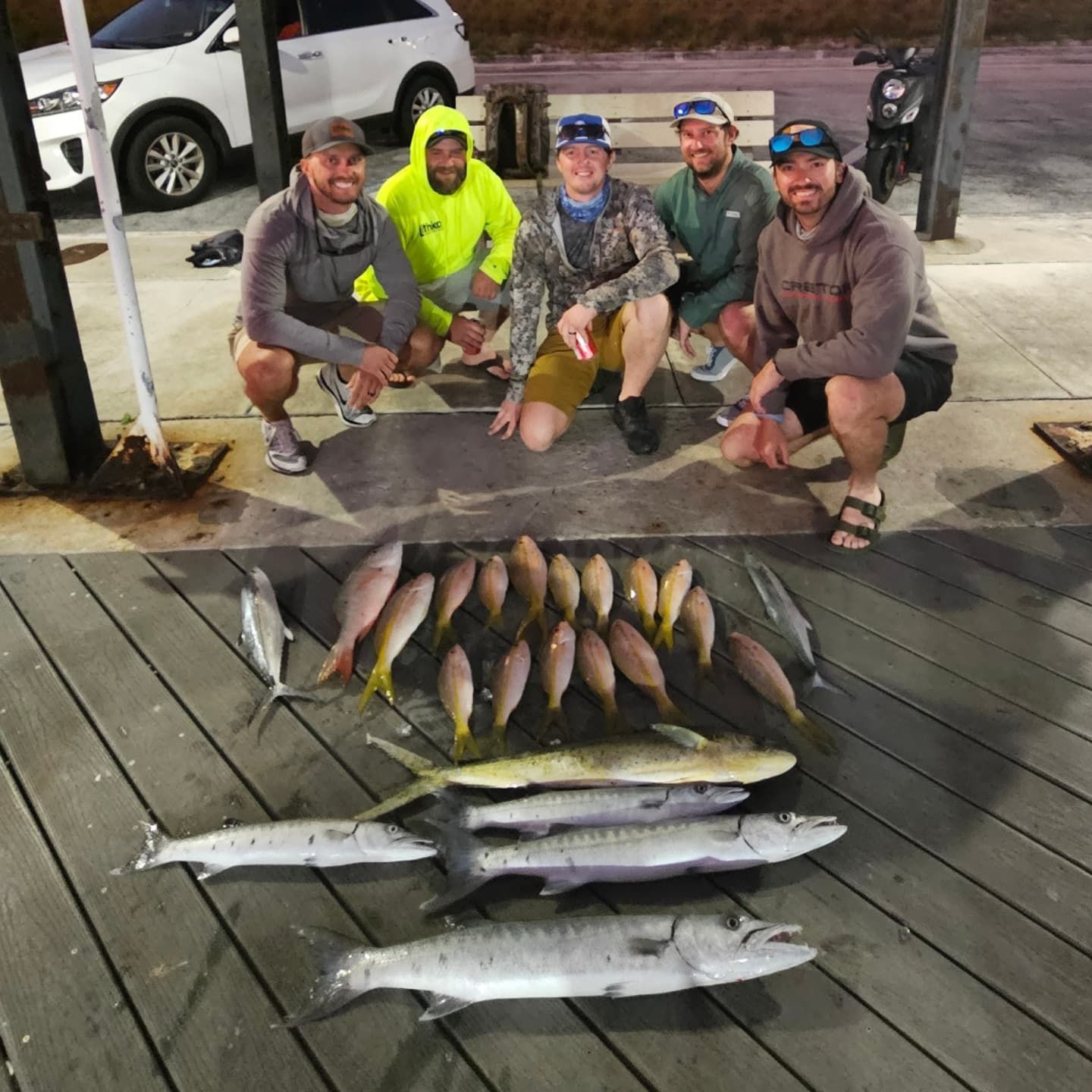 Five people pose behind a large collection of fish laid out on a wooden pier at night.