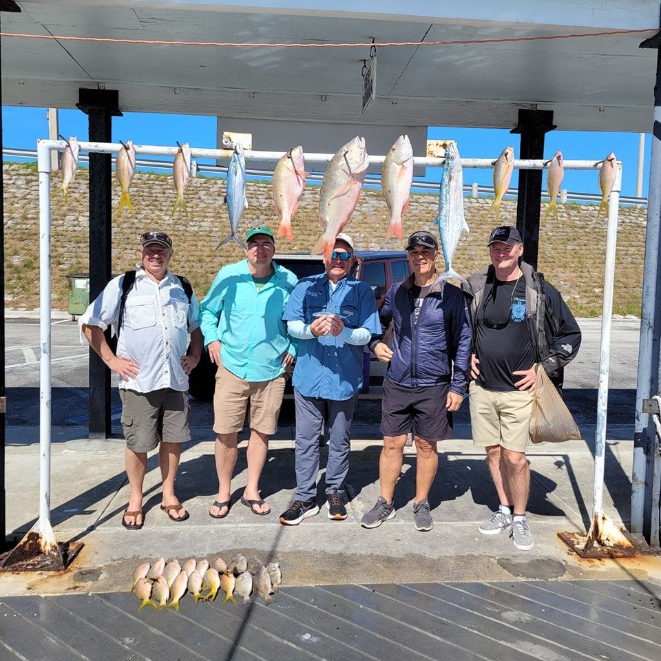 Five people stand beneath a cleaning station with a large catch of fish hanging from a metal frame and on the ground.