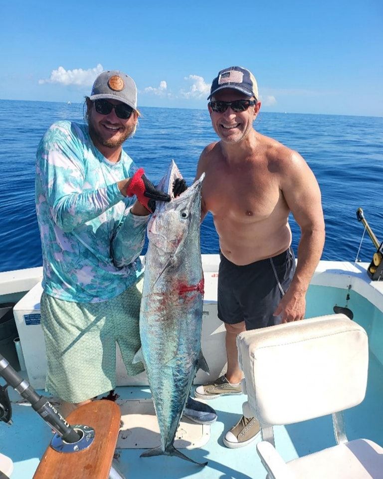 Two people stand on a boat on the ocean holding a large, caught fish between them.